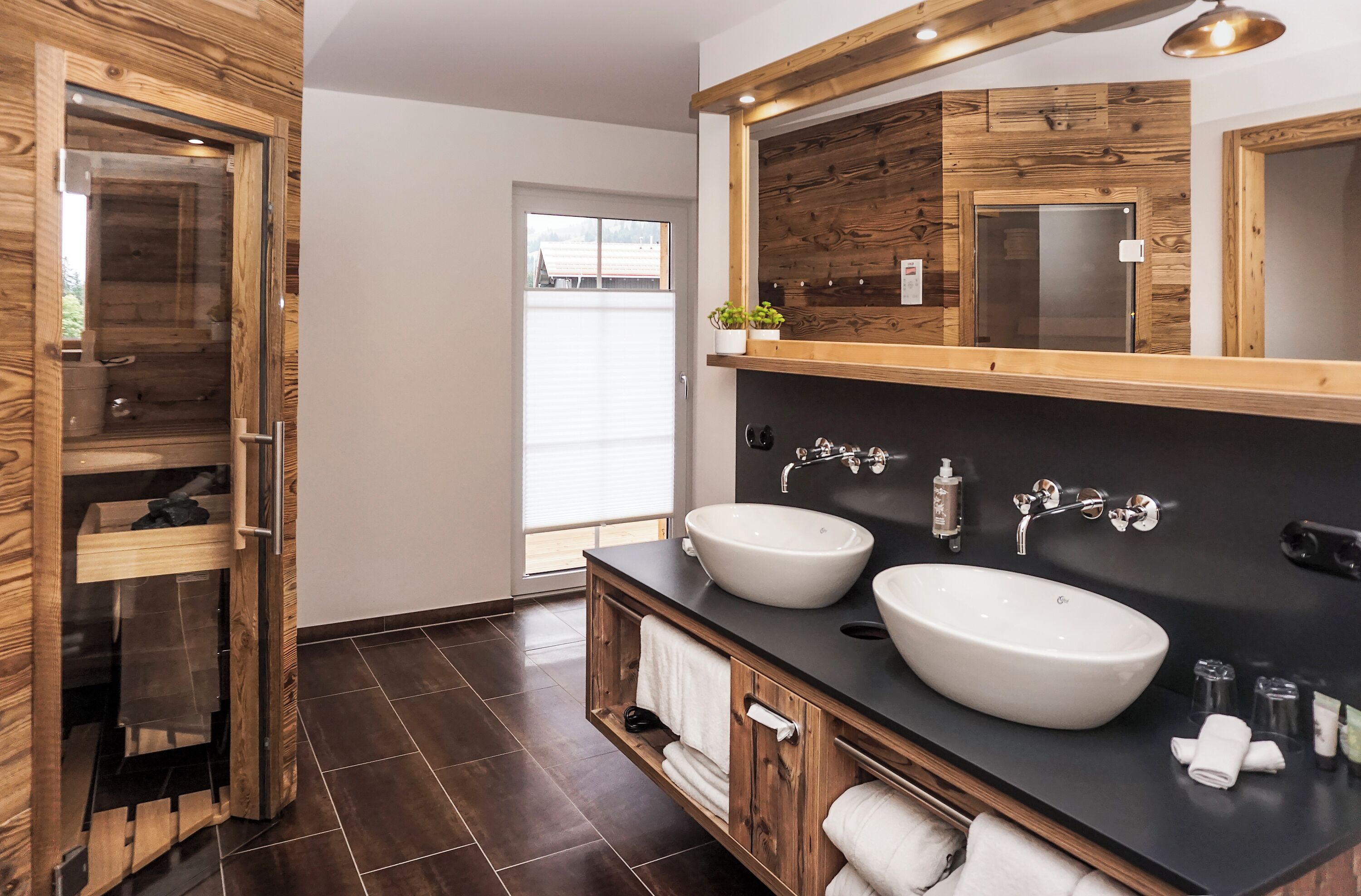A modern bathroom with two large sinks, wooden cabinetry, a large mirror, and a glass shower enclosure.