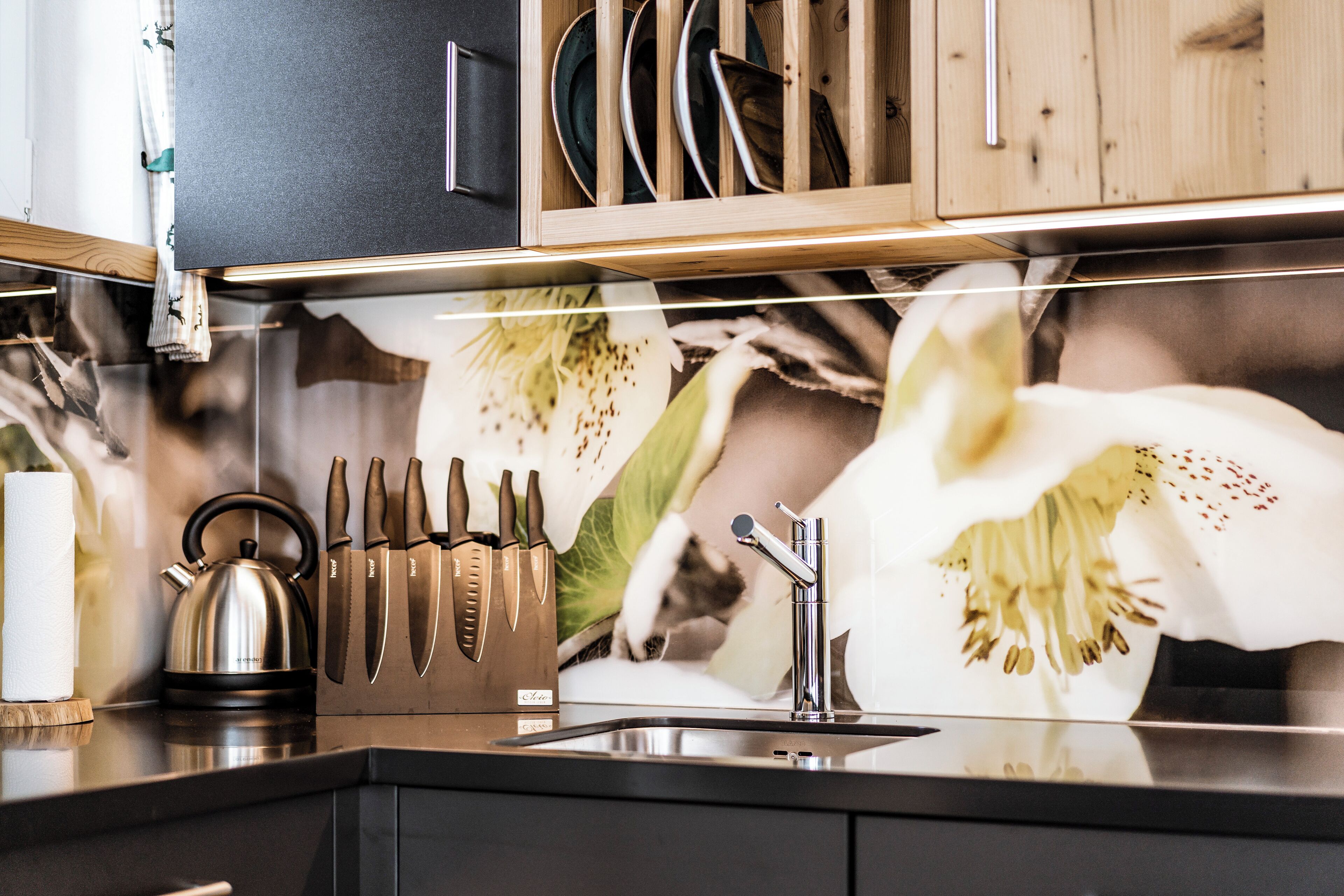 Una cocina con un hervidor de acero inoxidable, un bloque de cuchillos y un lavamanos.