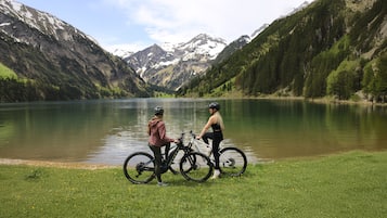 Two people on bicycles by a lake with mountains in the background.
