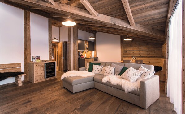 Una sala de estar acogedora con un sofá seccional, vigas de madera en el techo y una pequeña kitchenette.