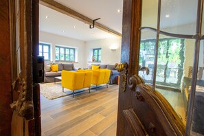 Une vue intérieure d’une pièce avec une porte en bois, un ensemble de meubles de salon et une grande fenêtre.