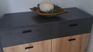 A wooden cabinet with two black handles, a woven basket on top with a white object and green plants, and a plain white wall in the background. - Apartment in the Ries with Wi-Fi (Wallerstein)