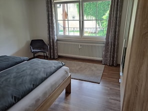 Une chambre à coucher avec un lit, une chaise, un radiateur et une fenêtre avec des rideaux.