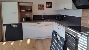 A compact kitchen with a built-in oven, a sink, and a dining area with a table and chairs. - Apartment in the Ries with Wi-Fi (Wallerstein)