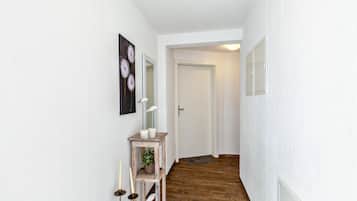 Un corridoio con pavimento in legno, una porta bianca, un piccolo tavolo consolle in legno con una pianta e specchi a parete.
