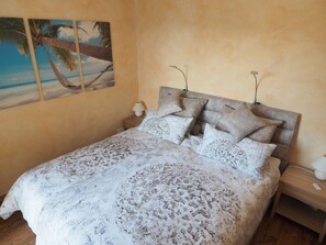 A bedroom with a bed, pillows, a nightstand, a lamp, and a painting of a beach scene.
