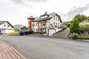 A residential street with a two-story house featuring a garage, a balcony, and a driveway. - Apartment 'Ferienwohnung Typ 1' with Mountain View, Shared Terrace and Wi-Fi (Willingen (Upland))