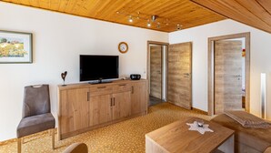 A modern room with a wooden ceiling, a television on a wooden cabinet, a clock on the wall, and a framed picture.