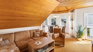 A spacious living area with a wooden ceiling, a sofa set, a coffee table, and a dining area with chairs and a table.