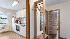 A modern kitchen with white cabinets, a microwave, and an oven. There is a wooden bench and a door leading to another room.