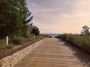 A wooden boardwalk leading to the beach, surrounded by sand and vegetation.