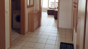 Um corredor com máquina de lavar, armário de madeira, porta com espelho e chão ladrilhado.