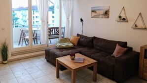 Uma sala de estar com um sofá marrom, uma mesa de centro de madeira, uma mesa de jantar com cadeiras e uma porta de vidro deslizante que dá para uma varanda.