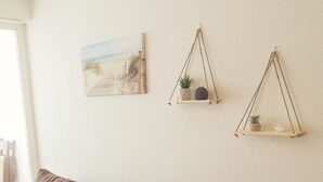 Um sofá de couro marrom com um travesseiro amarelo, uma mesinha de madeira com uma pequena planta, e uma prateleira na parede com duas plantas.