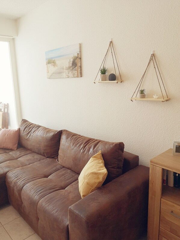 A brown leather sofa with a yellow pillow, a wooden side table with a small plant, and a wall-mounted shelf with two plants.