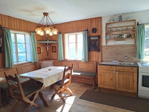 A cozy kitchen with wooden walls, a dining table with chairs, a hanging light fixture, and a window with curtains.