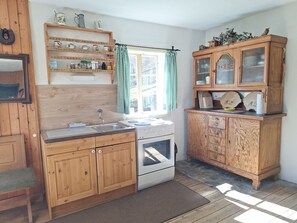 A kitchen with wooden cabinets, a sink, a stove, and a window with checkered curtains.