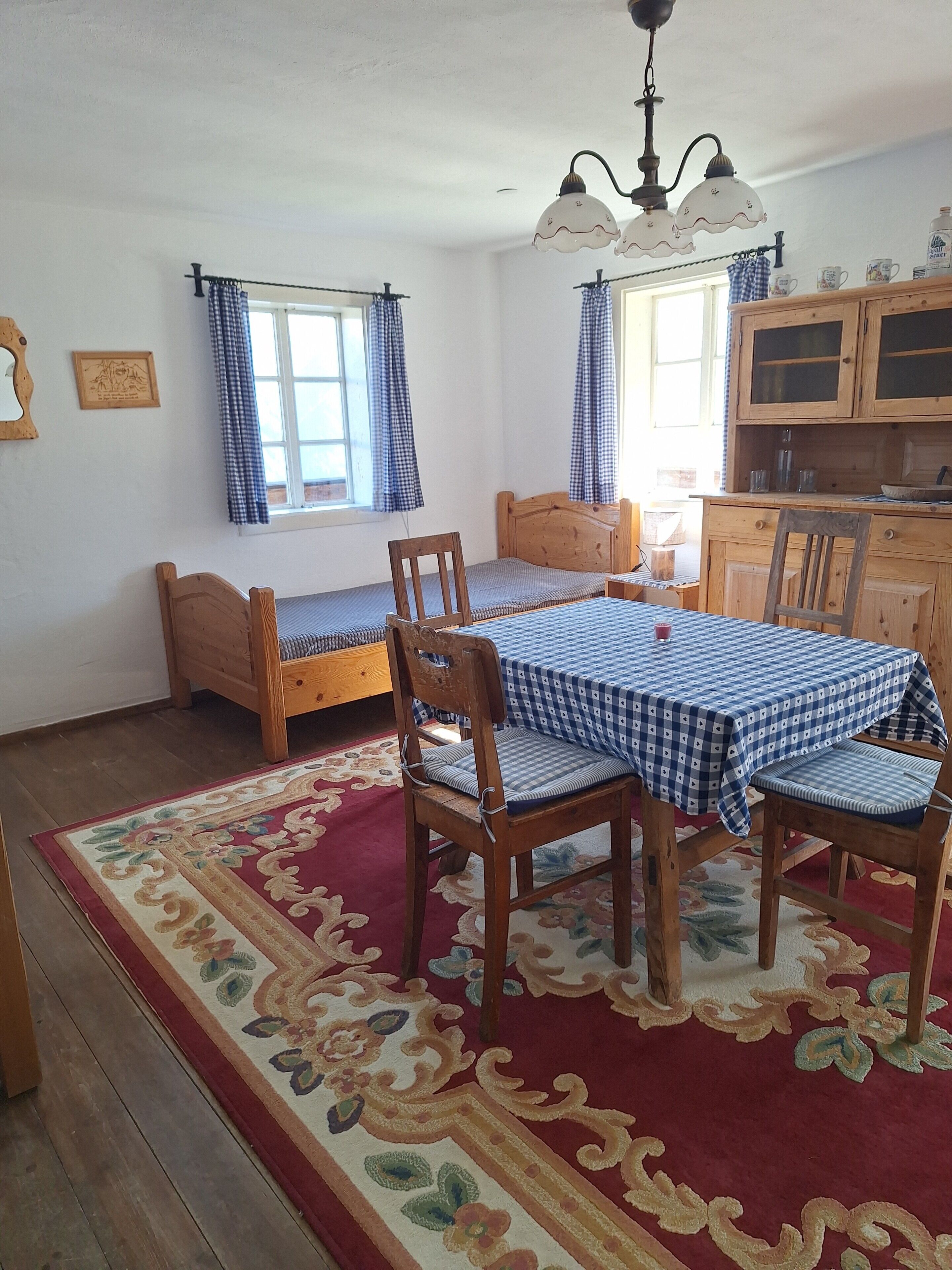 Una habitación con una cama, una mesa con sillas, un tapete, una ventana con cortinas y un armario.