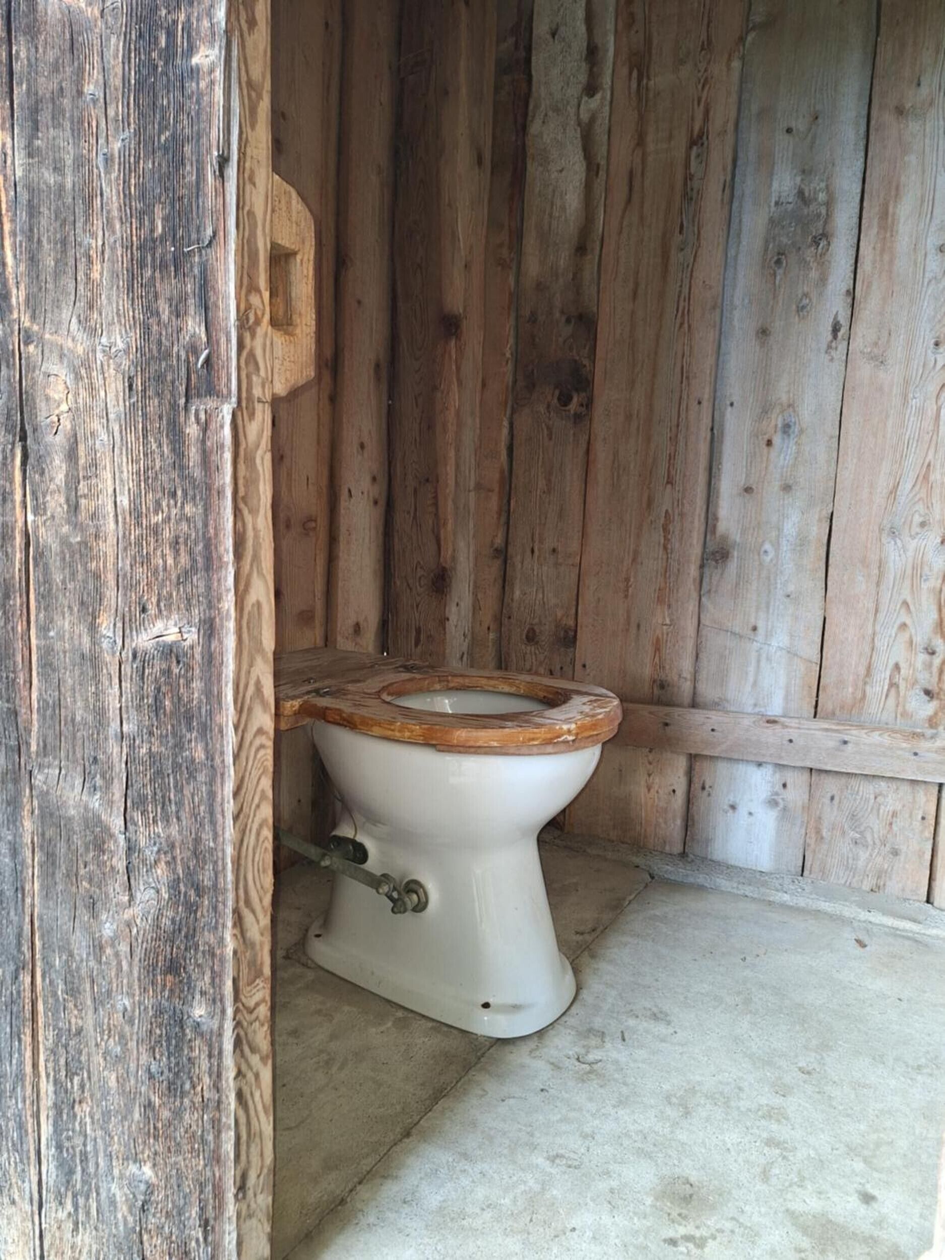 Un bagno rustico in legno, con lo scafo del water in legno e un tubo metallico.