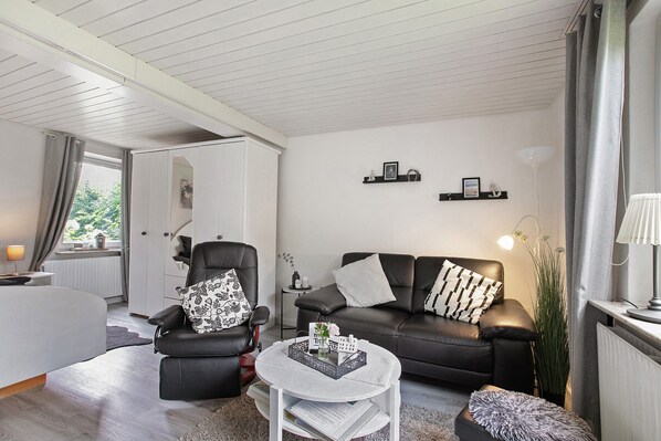 A modern living room with a sofa, armchair, and coffee table, a window with curtains, and a radiator.