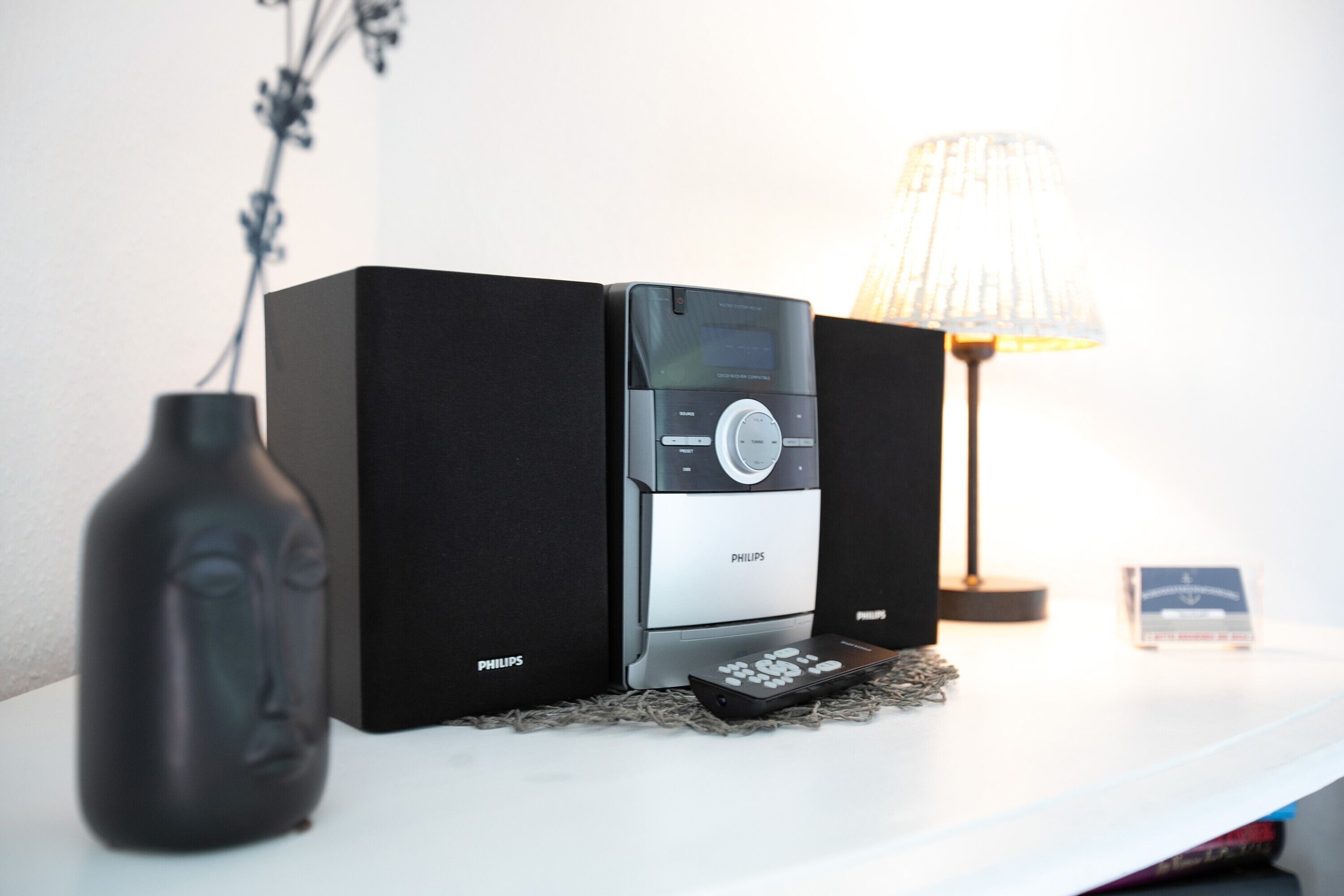 A Philips audio system on a white surface with a vase and a lamp.