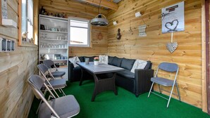 Een houten blokhut van binnen met een bank, stoelen, een tafel en een groen vloerkleed.