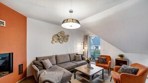 A modern living room with a sectional sofa, a coffee table, and two armchairs. A unique ceiling design and a decorative wall piece are visible.
