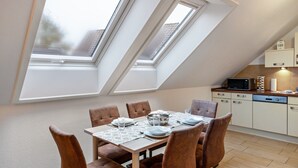 A dining area with a table set for four, a kitchen with appliances, and skylights.