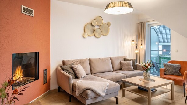 A living room with a sofa, a coffee table, a fireplace, and a view of the outside.