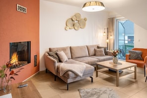 Ein Wohnzimmer mit einer Couch, einem Couchtisch, einem Kamin und Blick ins Freie.