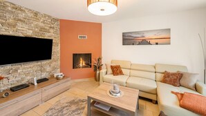 Een woonkamer met een flatscreen televisie, stenen muur, open haard, bank en een schilderij.