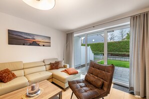 A modern living room with a sofa, armchair, and a painting on the wall. - Apartment 'Domizil Eden - Erdgeschoss' with Private Terrace, Private Garden and Wi-Fi (Göhren-Lebbin)