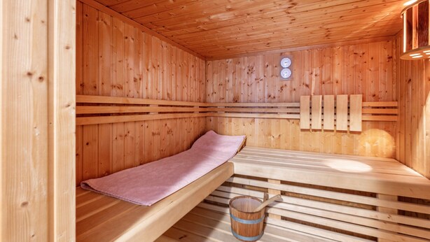 Een houten sauna met banken, een houten emmer en een handdoek.