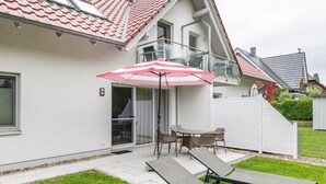 Een huis met een terras, een tafel met stoelen en twee comfortabele fauteuils.