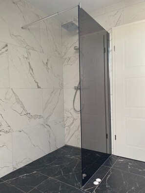 Une salle de bain moderne avec une douche à l’italienne en verre, des murs en marbre et un sol carrelé foncé.