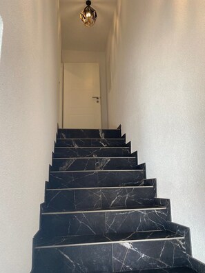 Un escalier avec des marches en marbre noir et un luminaire au design géométrique.