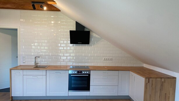 Una cocina moderna con armarios blancos, horno integrado y encimera de madera.