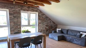 Una habitación estilo loft con una mesa de comedor de madera, dos sillas, un sofá gris y una pared de ladrillo.