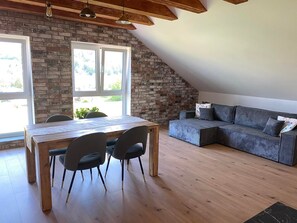 Une pièce de style loft avec une table à manger en bois, deux chaises, un canapé gris et un mur en briques.
