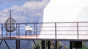 Una struttura a forma di cupola con tetto trasparente, una scultura metallica sferica e un'area salotto con sedie.