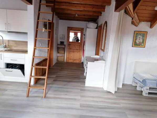 A narrow hallway with a wooden ladder, white cabinets, a white sink, and a bed with striped bedding.