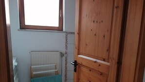 Una habitación con puerta de madera, un radiador, una ventana y una toalla sobre un soporte.