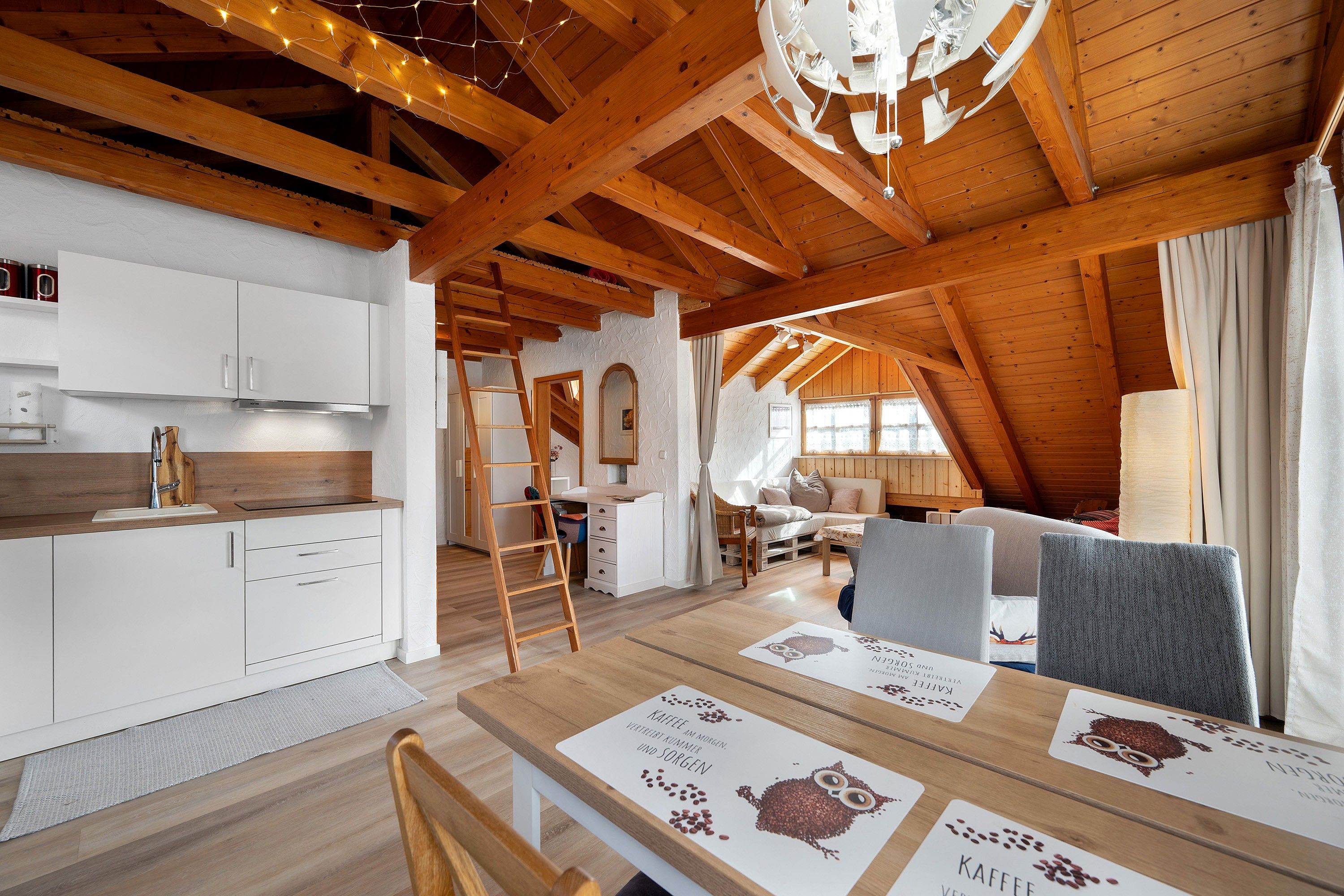 A cozy, rustic interior with a wooden ceiling, a kitchen area, and a dining space with a table set for two.