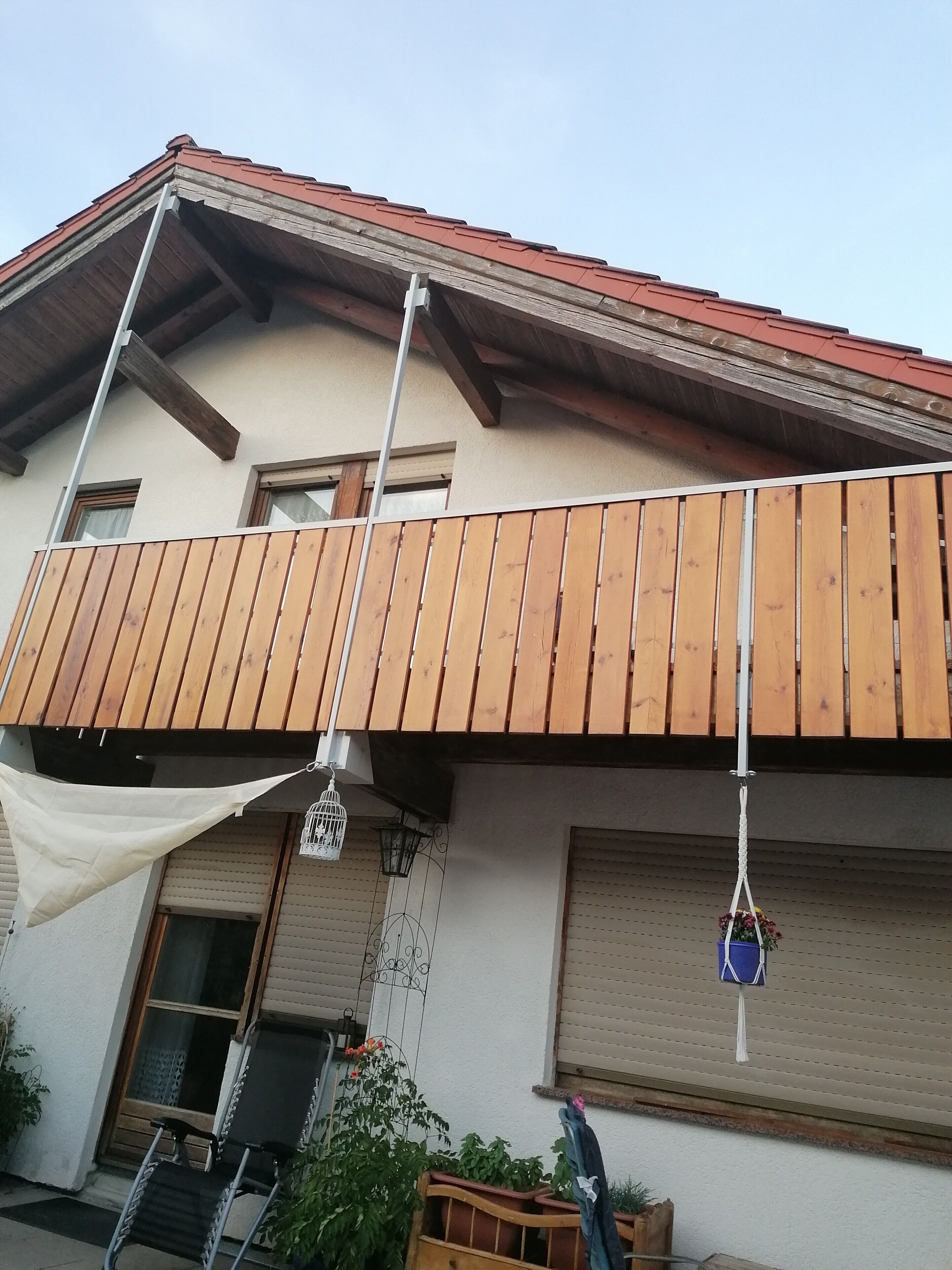 Een gebouw met twee verdiepingen, een balkon, een houten hek en een wit zonnescherm.