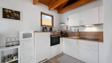 Une cuisine moderne avec des meubles blancs, un four encastré, une machine à café et une fenêtre donnant sur l’extérieur.