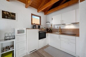 A modern kitchen with white cabinetry, a built-in oven, a coffee maker, and a window with a view of the outside.
