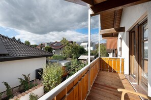 Un balcón con piso y barandilla de madera, con vista a una zona residencial con casas y un jardín.
