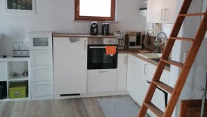 Una cocina con armarios blancos, techo de madera, una ventana y una escalera de madera.