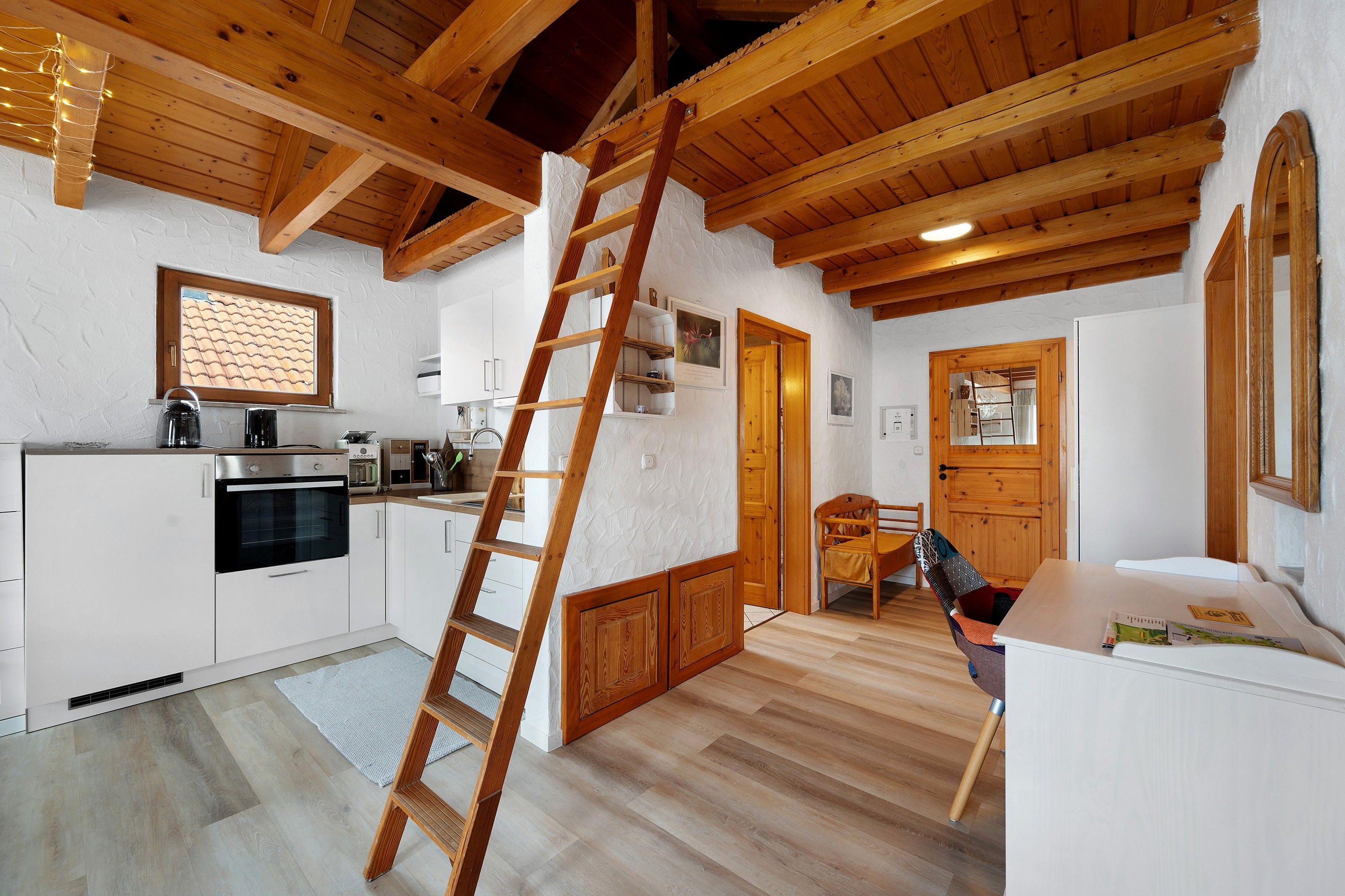 A modern kitchen with white cabinets, a stainless steel oven, and a wooden ladder.