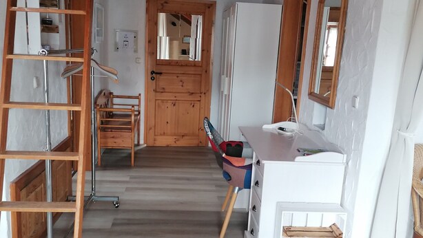 Una habitación con una escalera de madera, un escritorio, una silla y una puerta.